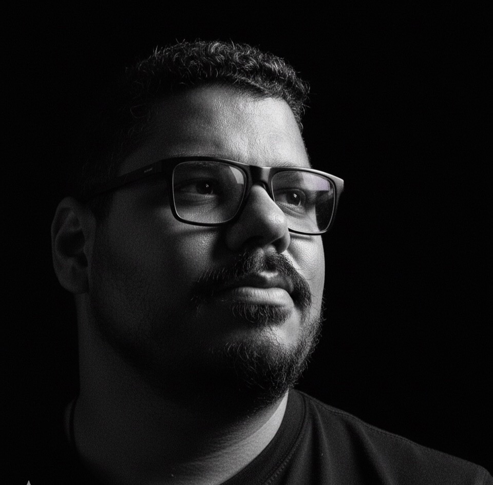 Retrato em preto e branco do Ari, de óculos, olhando para o alto, com o rosto iluminado de lado e o resto no escuro.